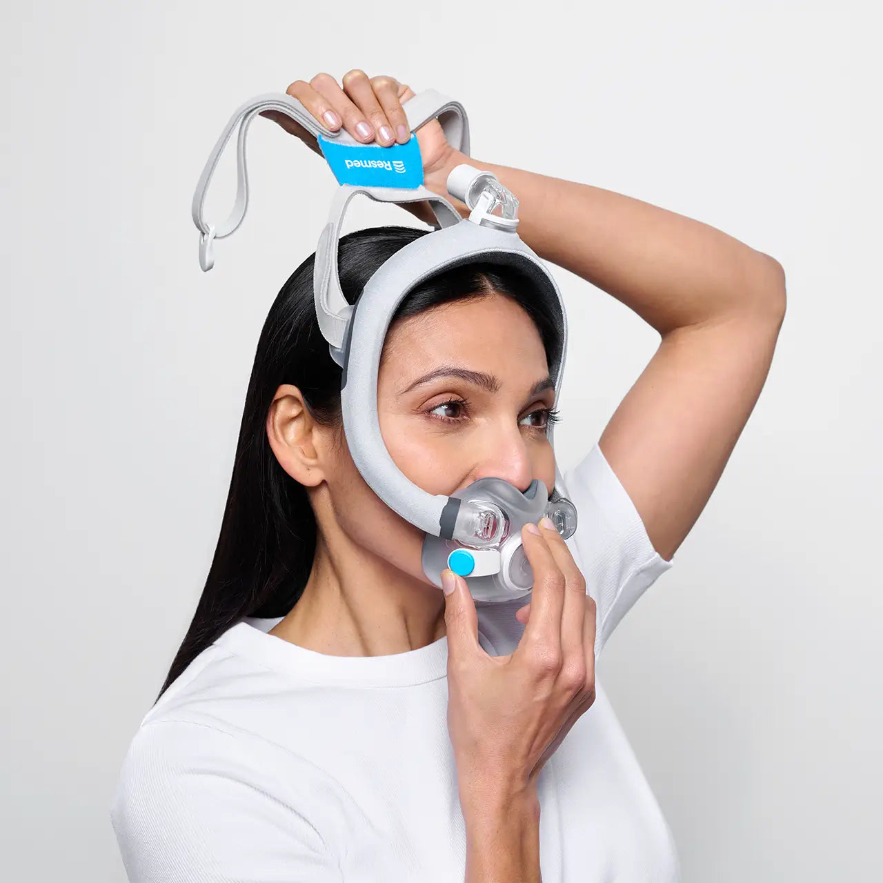 Woman is putting on the F30i, she is standing to the side. pulling the front first and the back of the mask second
