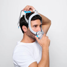 Man putting on the F30i CPAP mask, front first and and attaching the back.